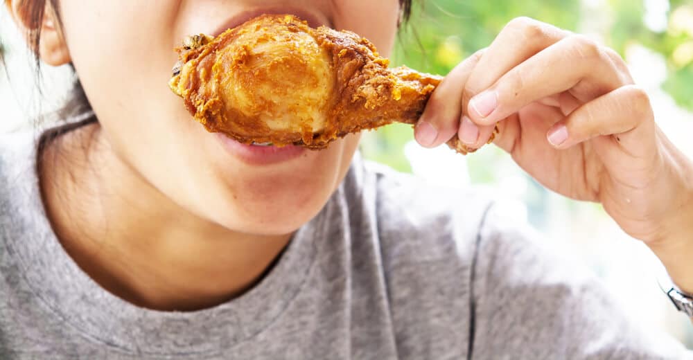Lady biting into an unhealthy, fried drumstick